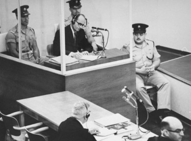 Eichmann em seu julgamento em Israel em  maio de 1961, com seu advogado Robert Servatius (centro) e o promotor Gideon Hausner (canto direito). Fonte:  United States Holocaust Memorial Museum.